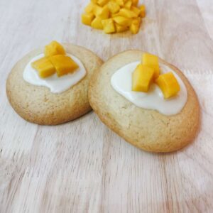 Bánh cookie mềm nhân xoài với lớp vỏ vàng và phần nhân xoài chảy, đặt trên nền pastel vàng, thương hiệu Mimi Bakes