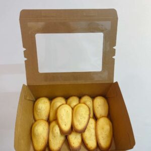 Hộp bánh với 12 madeleines vàng ruộm trong giấy lót, đặt trên nền màu pastel
