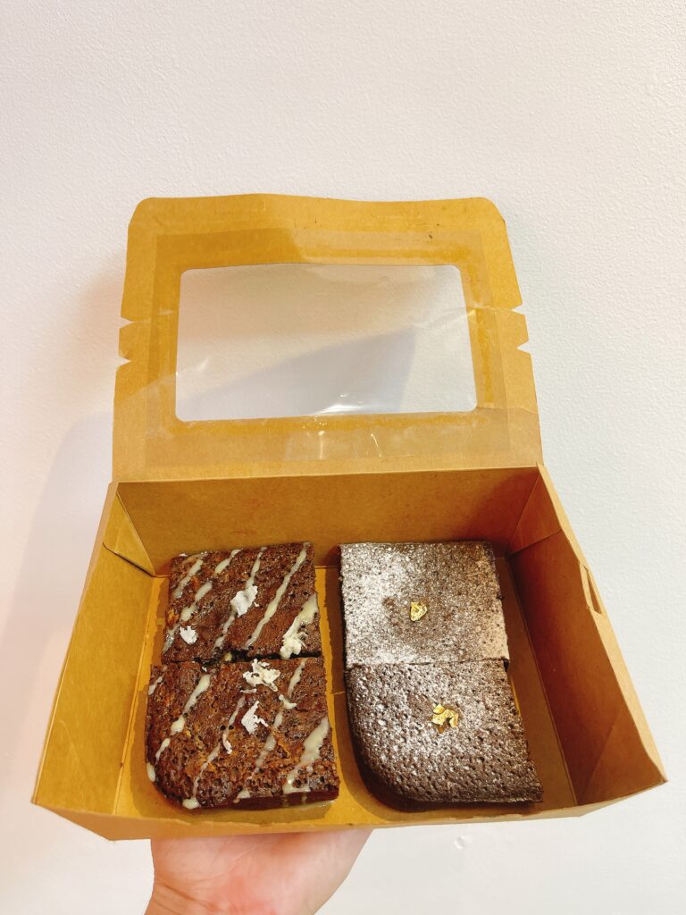 Hộp kraft chữ nhật nhỏ chứa 2 brownie socola đen và 2 brownie phủ dừa, đặt trên nền pastel kem, logo Mimi Bakes