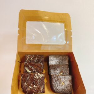 Hộp kraft vuông chứa 6 miếng brownie: 3 socola đen, 3 phủ dừa nạo, bên cạnh là hoa cúc trắng, nền màu nâu pastel