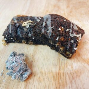 Miếng brownie vuông mềm ẩm với lớp mặt hơi nứt và dừa nạo rắc trên, logo Mimi Bakes, nền pastel nâu