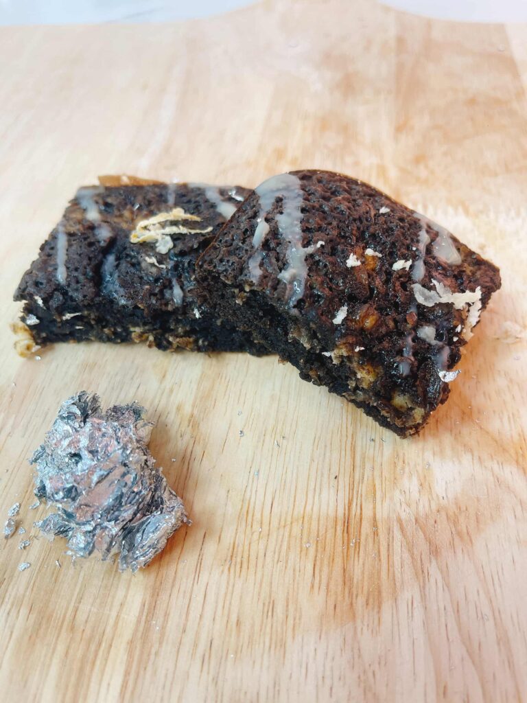 Miếng brownie vuông mềm ẩm với lớp mặt hơi nứt và dừa nạo rắc trên, logo Mimi Bakes, nền pastel nâu